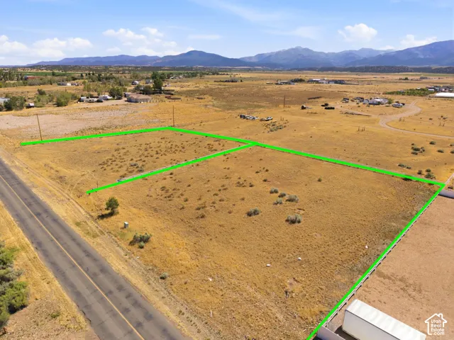 Expansive undeveloped land featuring a paved road frontage, natural vegetation, and distant mountain backdrops