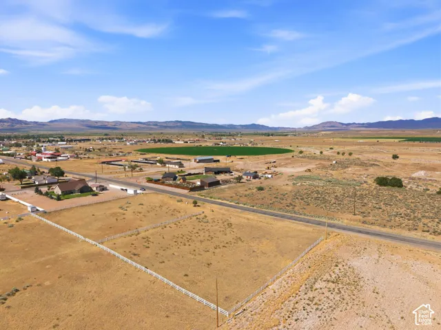 Expansive undeveloped land featuring a white perimeter fence, paved road frontage, and distant mountain vistas under a clear sky