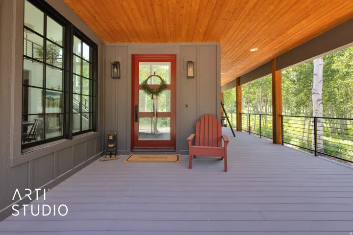Expansive covered porch featuring wood-finish ceiling, grey siding, and a red entry door