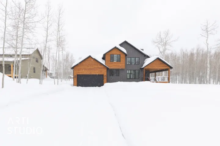 Modern architectural home with a dark gray exterior, wood paneling accents, multiple windows, an attached garage, and a covered front porch