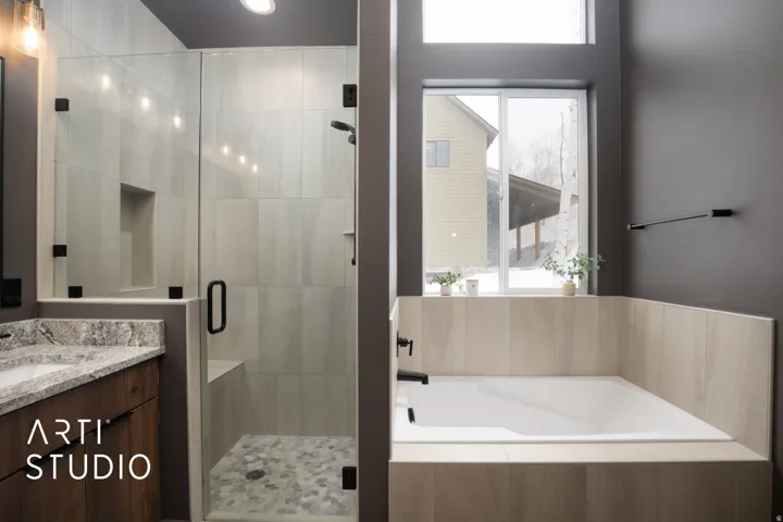 Contemporary bathroom featuring a spacious walk-in shower with a built-in bench and recessed niche, a separate soaking tub with surrounding light-toned tile, a vanity with a stone countertop, and matte black fixtures throughout