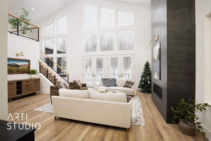 Vaulted living space featuring expansive windows, a tall dark-toned fireplace surround, light wood-finish flooring, a two-story staircase with dark metal railings, and a second-level open landing