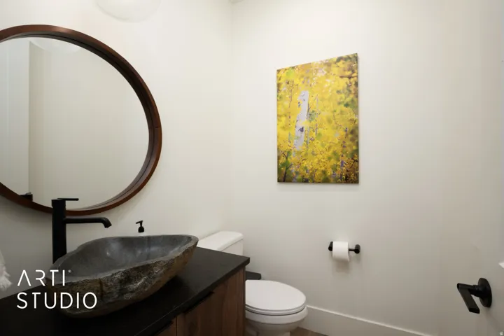 Modern powder room featuring a stone vessel sink, black matte faucet, wood-finish vanity, and a circular wood-frame mirror