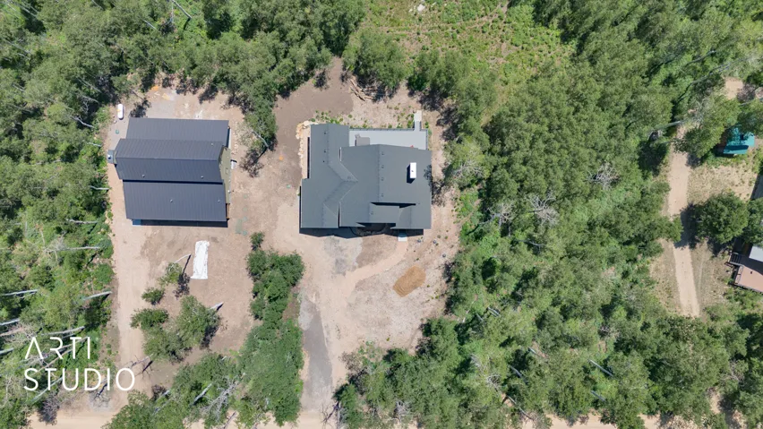 Aerial perspective showcasing a property featuring a main residence and a detached auxiliary structure, both with dark metal roofs