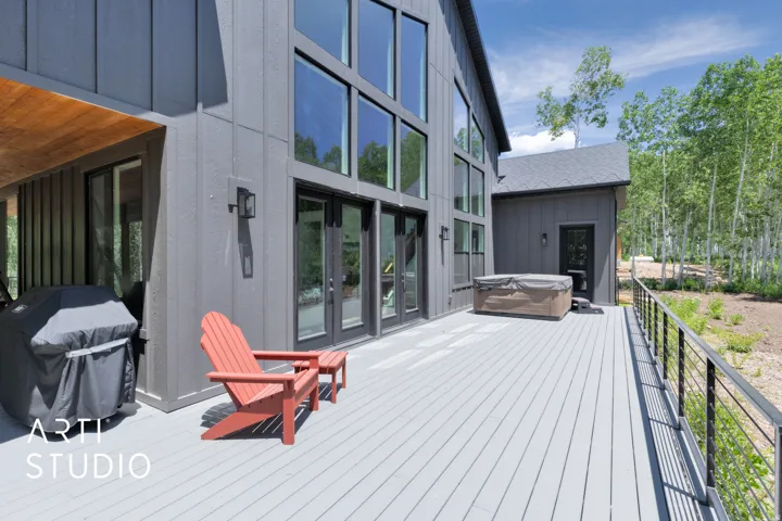 Expansive outdoor deck with composite decking, featuring a built-in hot tub, cable railing, and a covered grilling area with a wood-finish ceiling