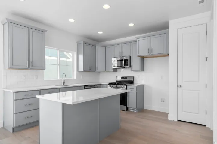 Kitchen featuring an island with a light-toned countertop, gray shaker-style cabinetry, white subway tile backsplash, and stainless steel appliances