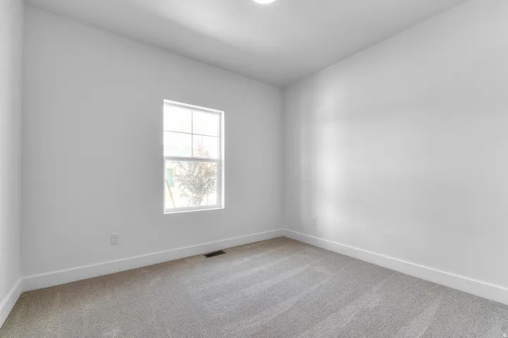 Neutral-toned room featuring a single window, light gray carpeting, crisp white walls, and matching white baseboards