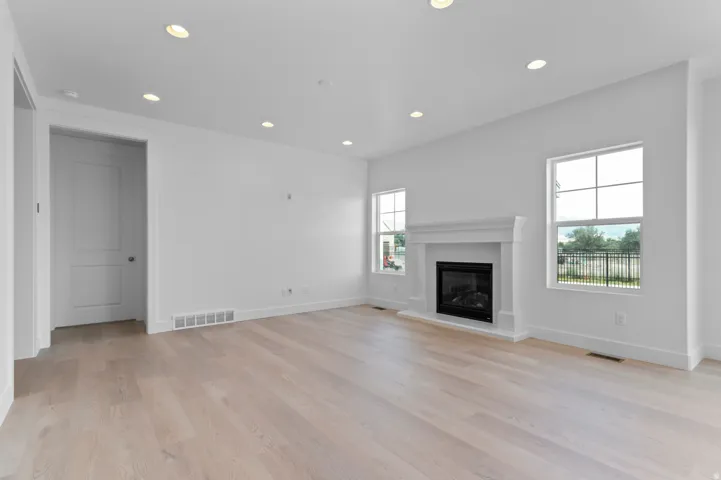 Spacious living area featuring light wood-finish flooring, a contemporary fireplace with a white mantel, and recessed ceiling lighting