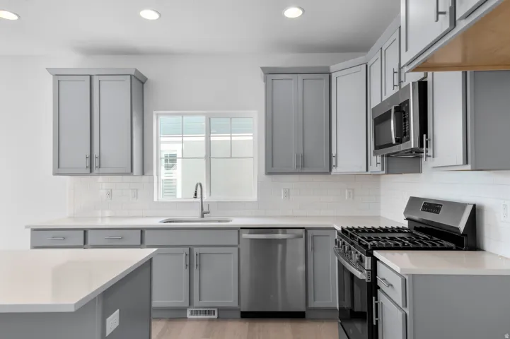Kitchen featuring gray shaker-style cabinetry, stainless steel appliances, white subway tile backsplash, and light-toned countertops