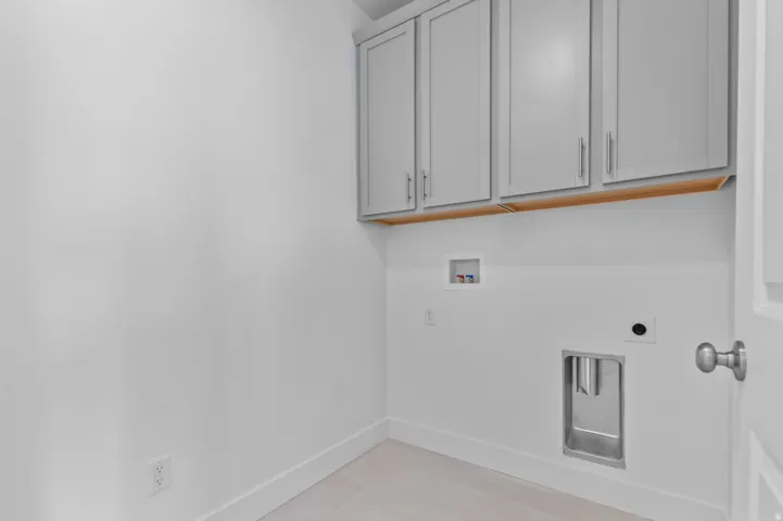 Laundry area featuring grey shaker-style cabinetry, wood-finish trim, and light-toned flooring