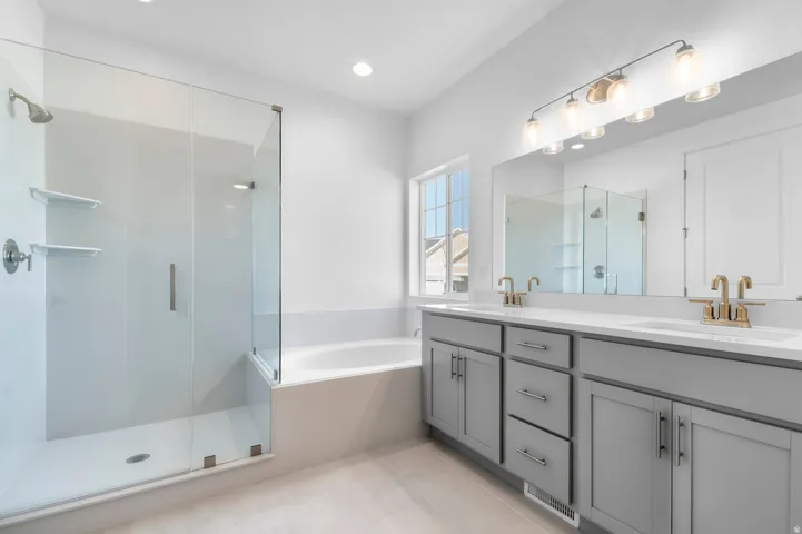 Contemporary bathroom featuring a glass-enclosed shower, built-in bathtub, dual vanity with light gray cabinetry, and brass-finish fixtures