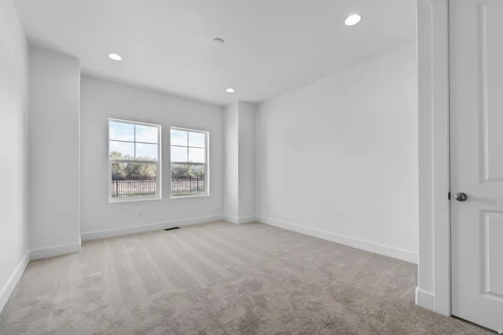 Bright room featuring two large windows, recessed ceiling lighting, light gray carpet, white baseboards, and a paneled interior door