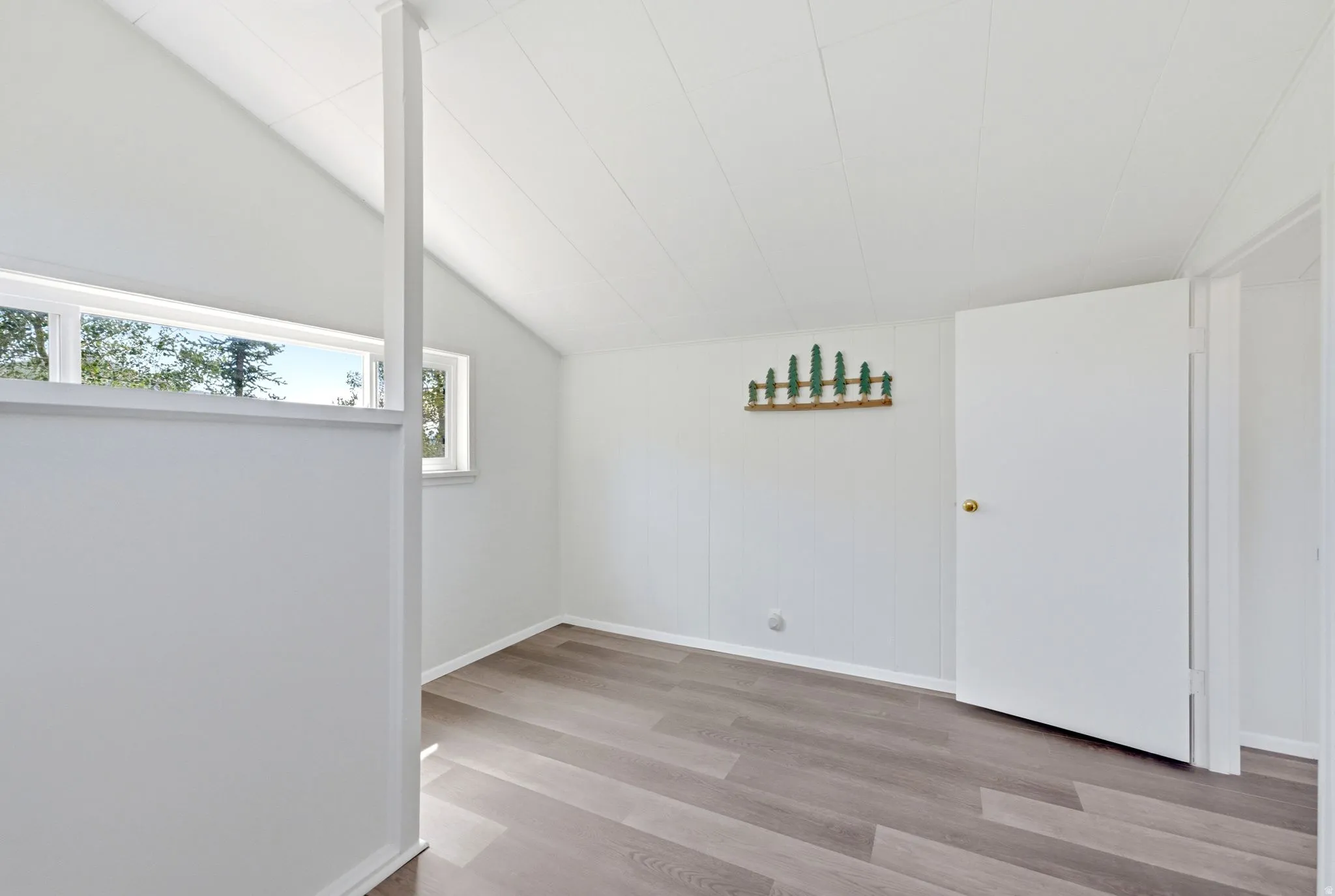 Room featuring wood-finish flooring, vaulted ceiling, and multiple windows