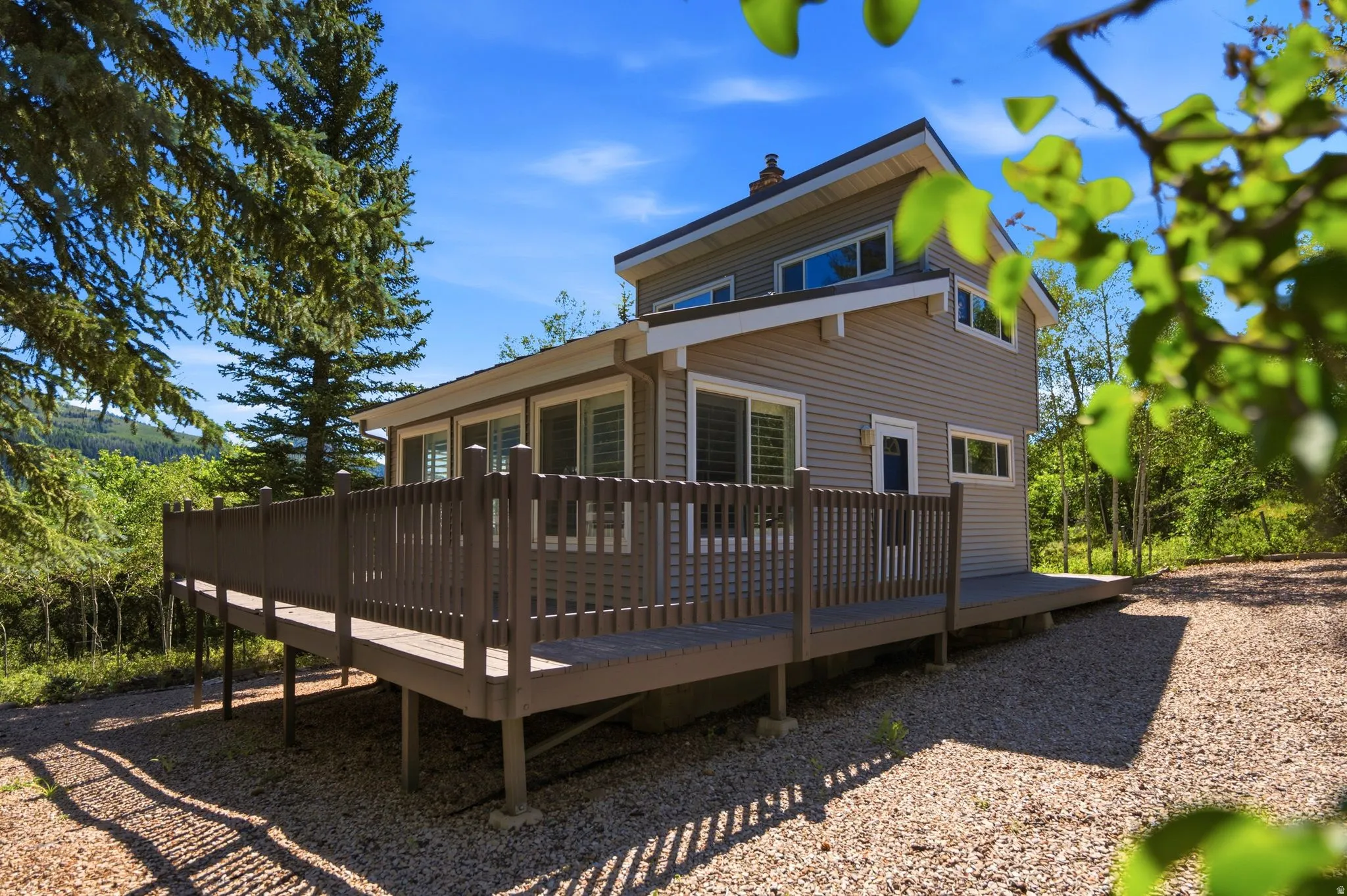 Multi-level home featuring horizontal siding, an expansive wrap-around deck, and a gravel ground cover