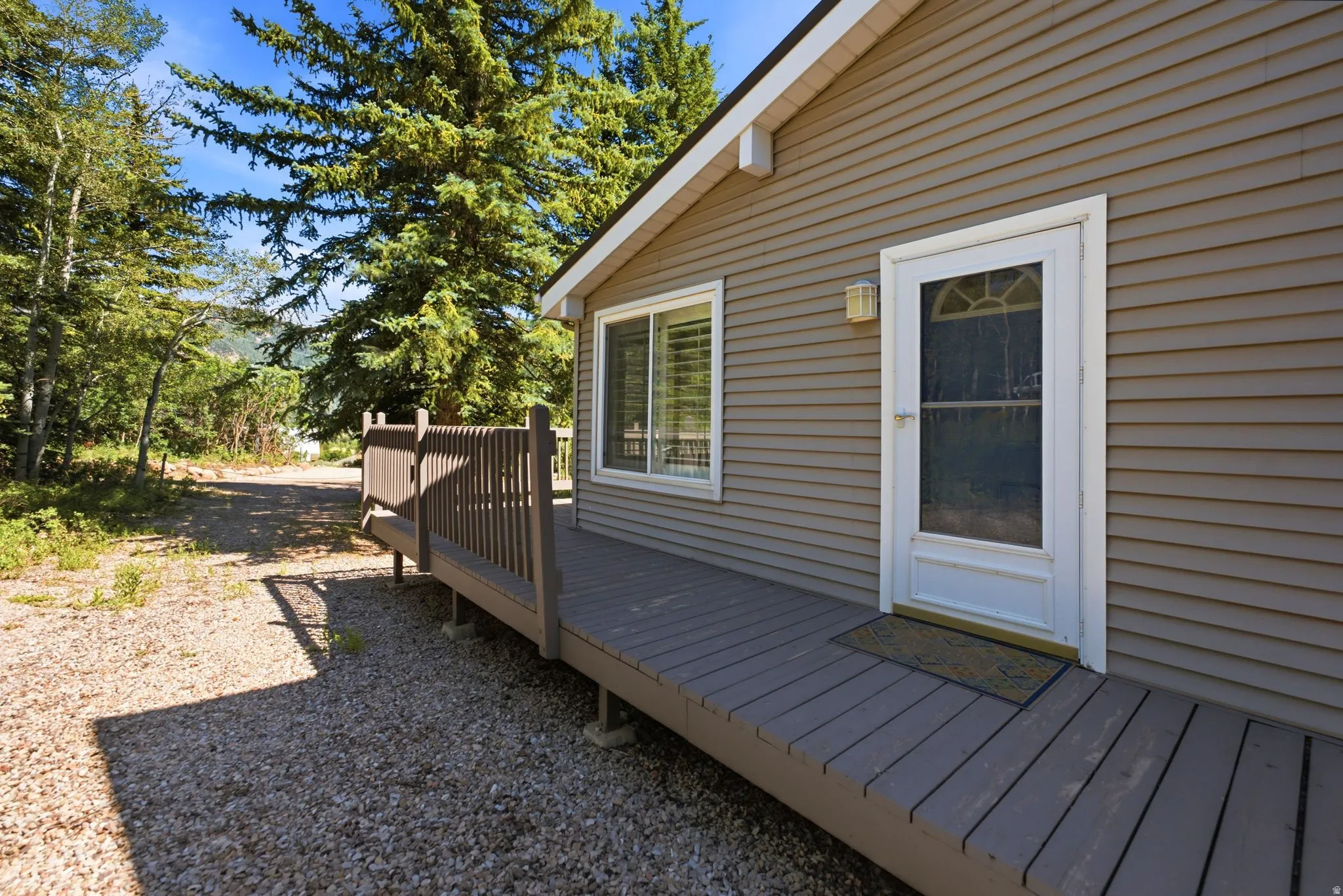 Exterior siding in a neutral tone complements a white-framed entry door with a storm door and transom window
