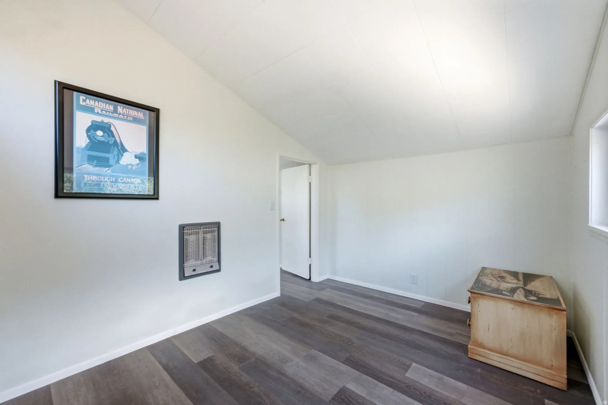 Room featuring wood-finish flooring, a wall-mounted heating unit, and a white interior door frame