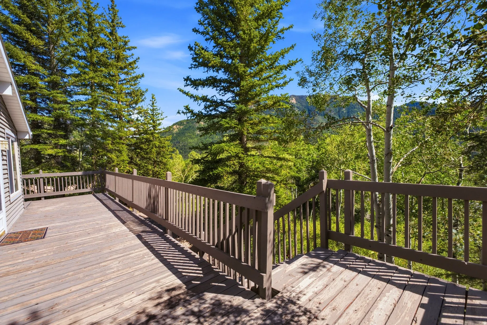 Expansive outdoor deck with wood railing, offering a natural treed backdrop and mountain scenery