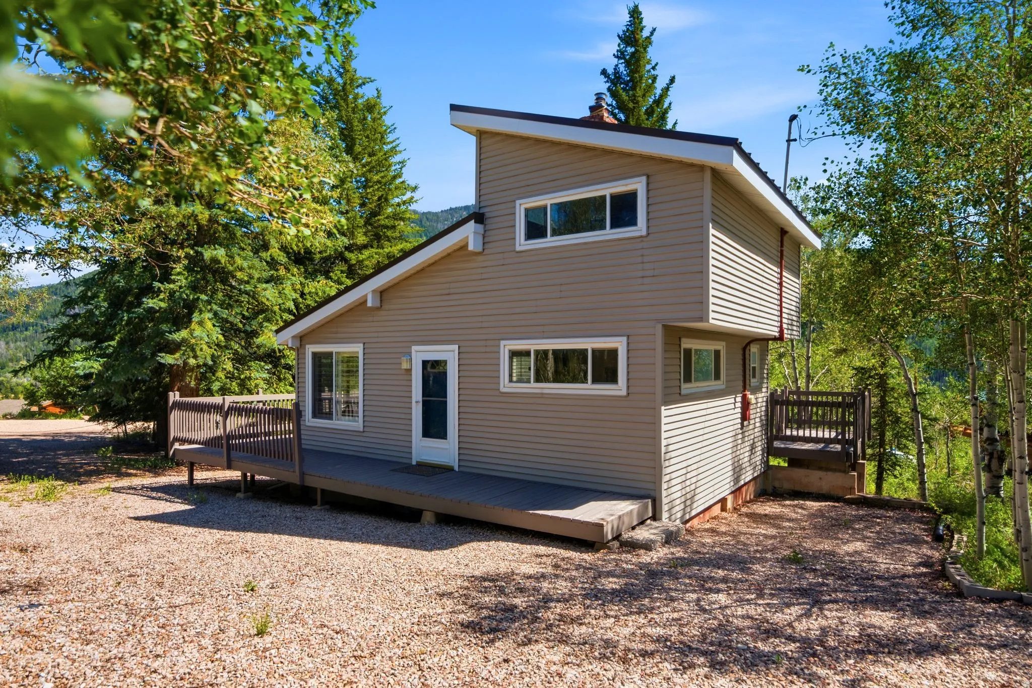 Contemporary architecture featuring neutral-toned siding, a multi-level deck, and a gravel driveway