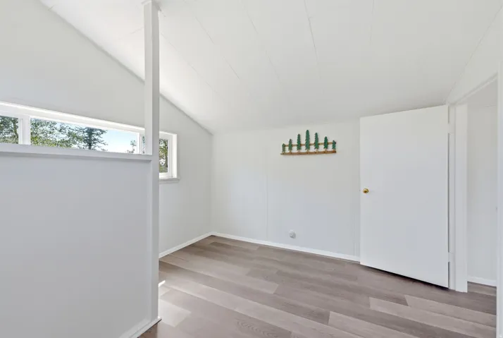 Room featuring wood-finish flooring, vaulted ceiling, and multiple windows