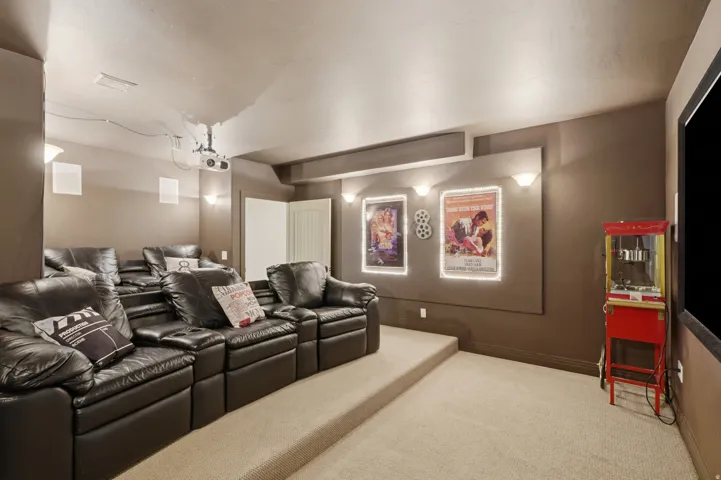 Dedicated media room featuring tiered carpeted flooring, a large projection screen, and wall-mounted sconces