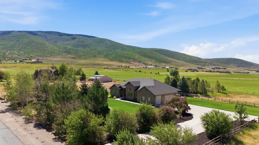 Expansive mountain landscape frames this property featuring a stone and stucco exterior, dark shingle roofing, an attached garage, and a concrete driveway