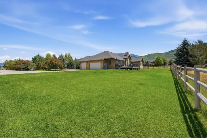Expansive green lawn with a split rail fence, backing onto a property featuring a multi-car garage, a rear deck, and mature trees