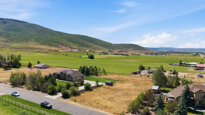 Expansive rural landscape featuring a single-family residence with an attached garage, a paved driveway, and mature landscaping