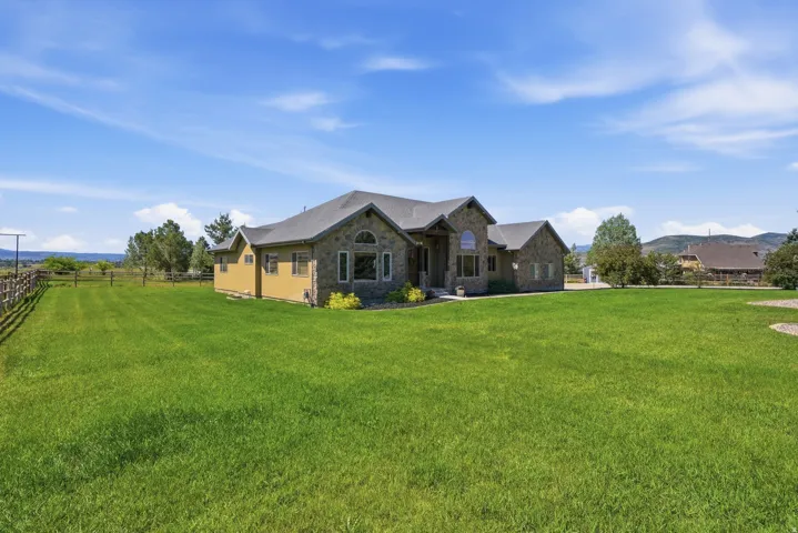 Spacious property featuring a stone and siding exterior, expansive green lawn, and a wooden perimeter fence