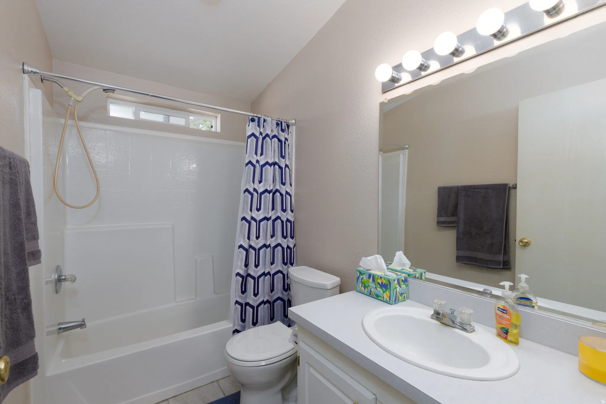 Bathroom featuring a bathtub with an integrated shower, a white vanity with a single sink, an expansive mirror, and overhead vanity lighting