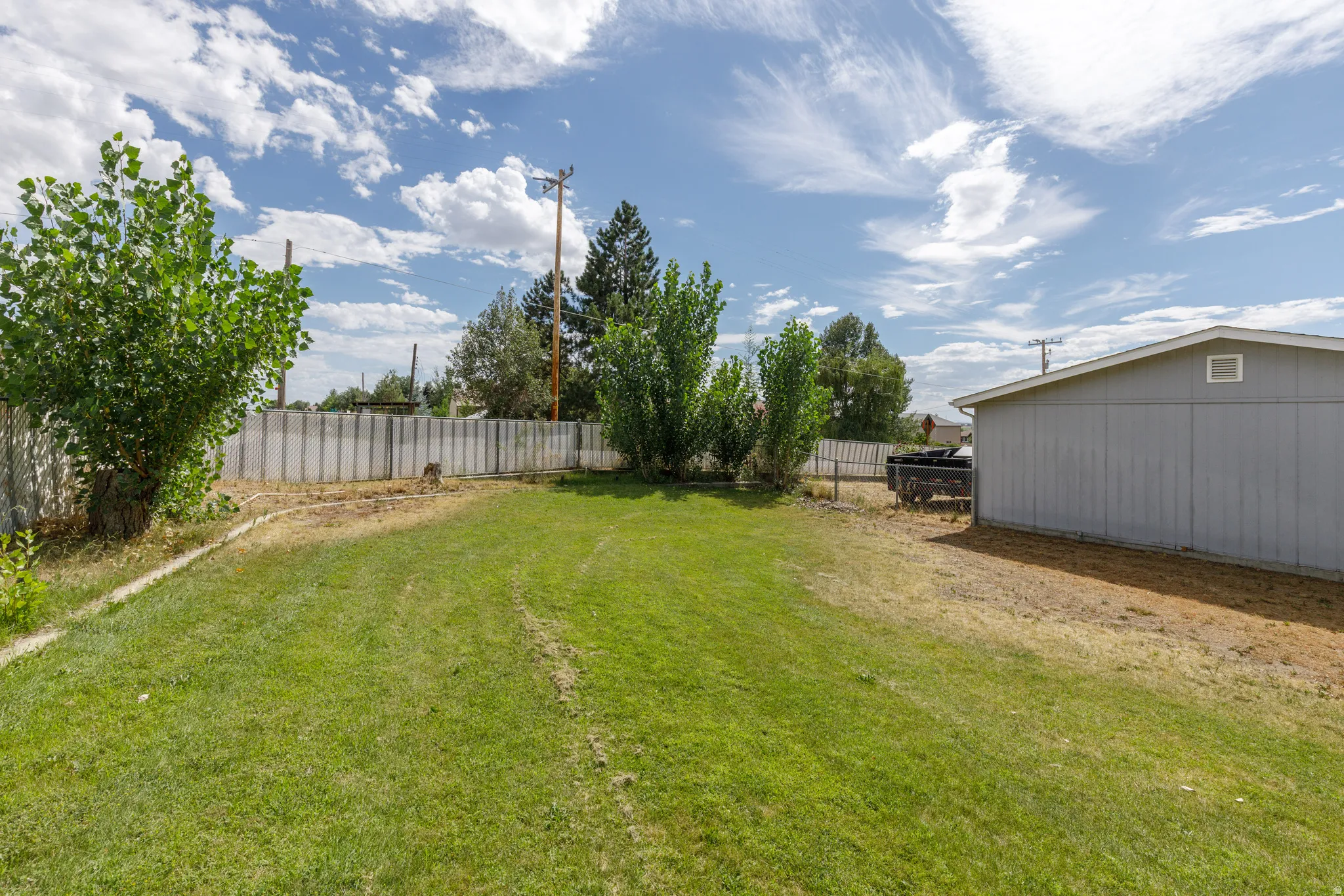 Expansive green lawn with a perimeter fence, mature trees, and a detached structure featuring gray siding