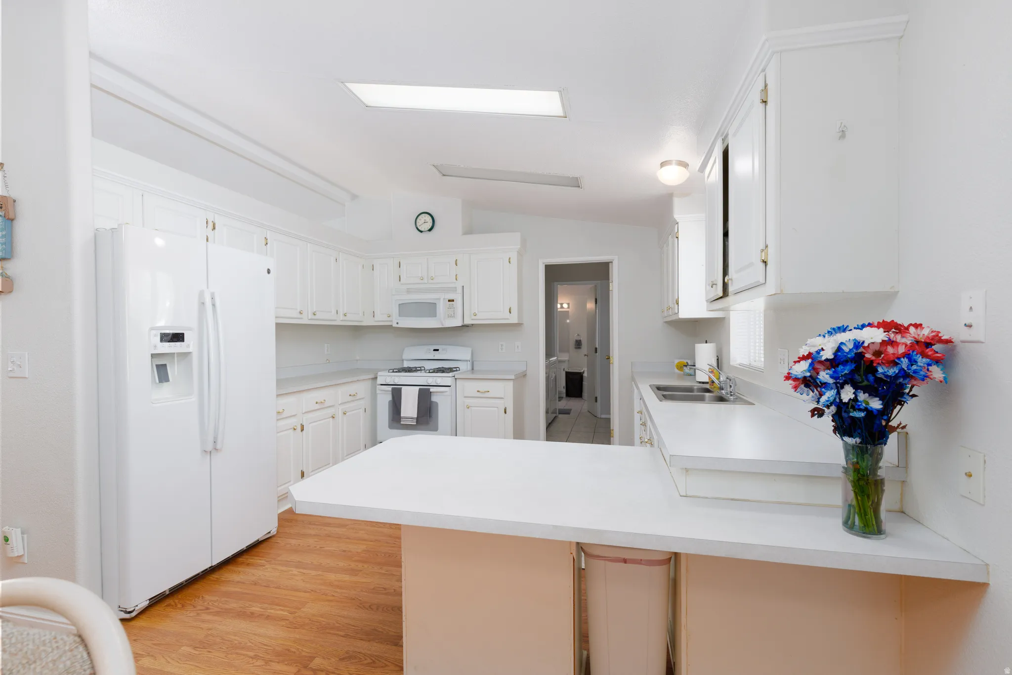 Kitchen featuring white cabinetry, white countertops, built-in microwave, gas range, and wood-finish flooring