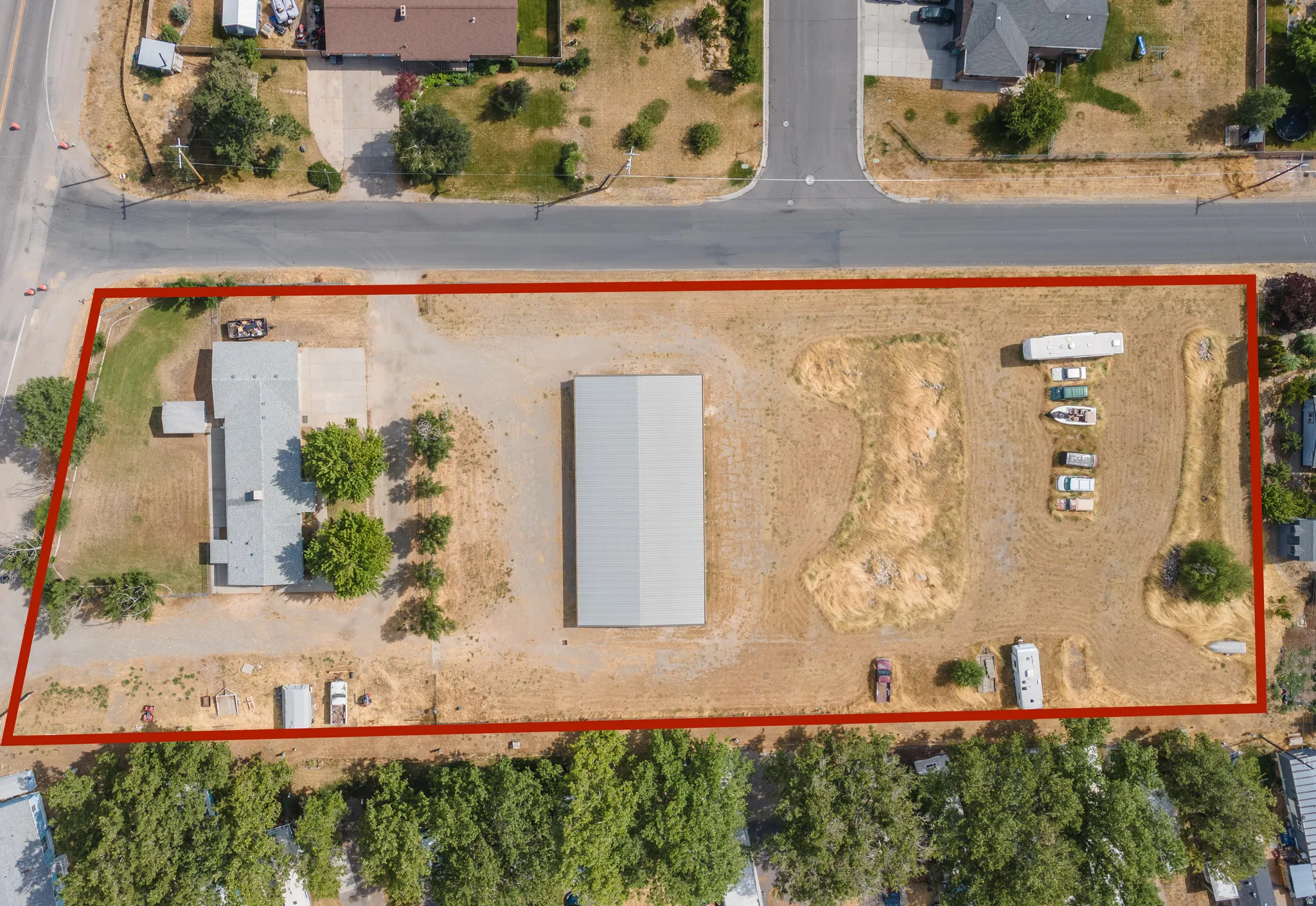 Expansive lot featuring a single-story residence, a large metal outbuilding, extensive unpaved areas, and mature trees