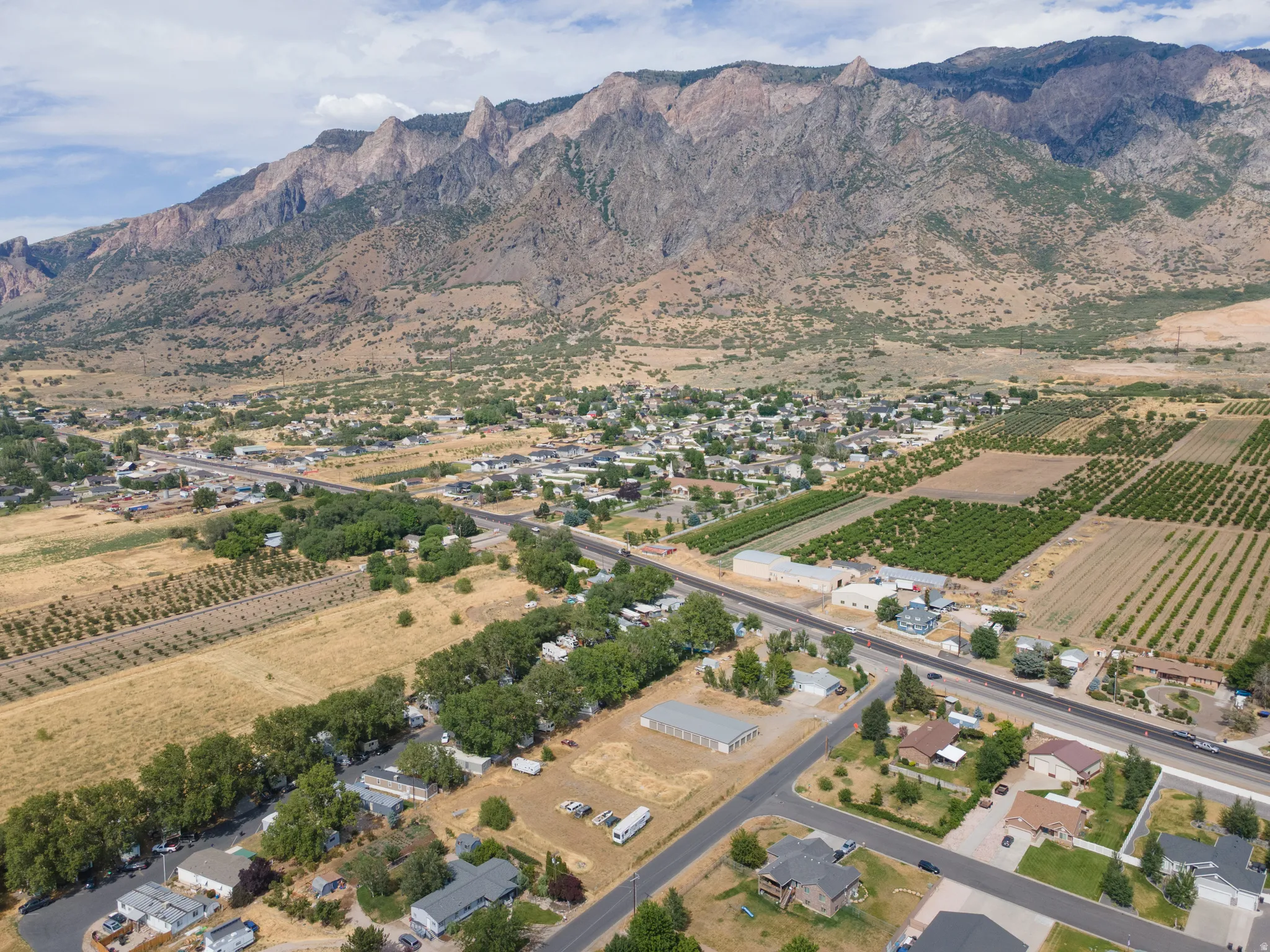 Expansive aerial perspective showcasing a mountainous backdrop, a residential community with mature trees, and agricultural fields