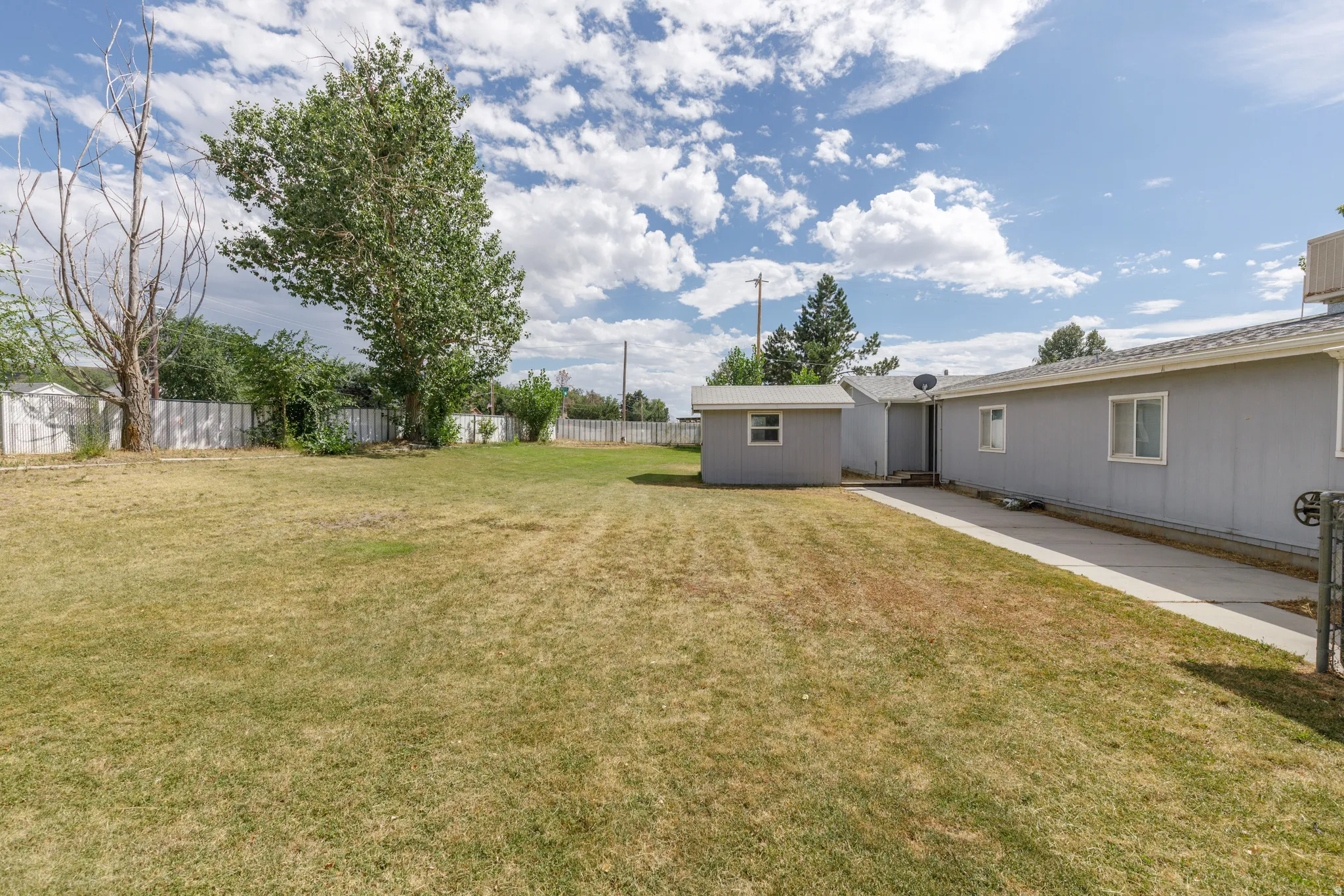 Expansive backyard featuring a large grass area, mature trees, a privacy fence, and a detached storage shed