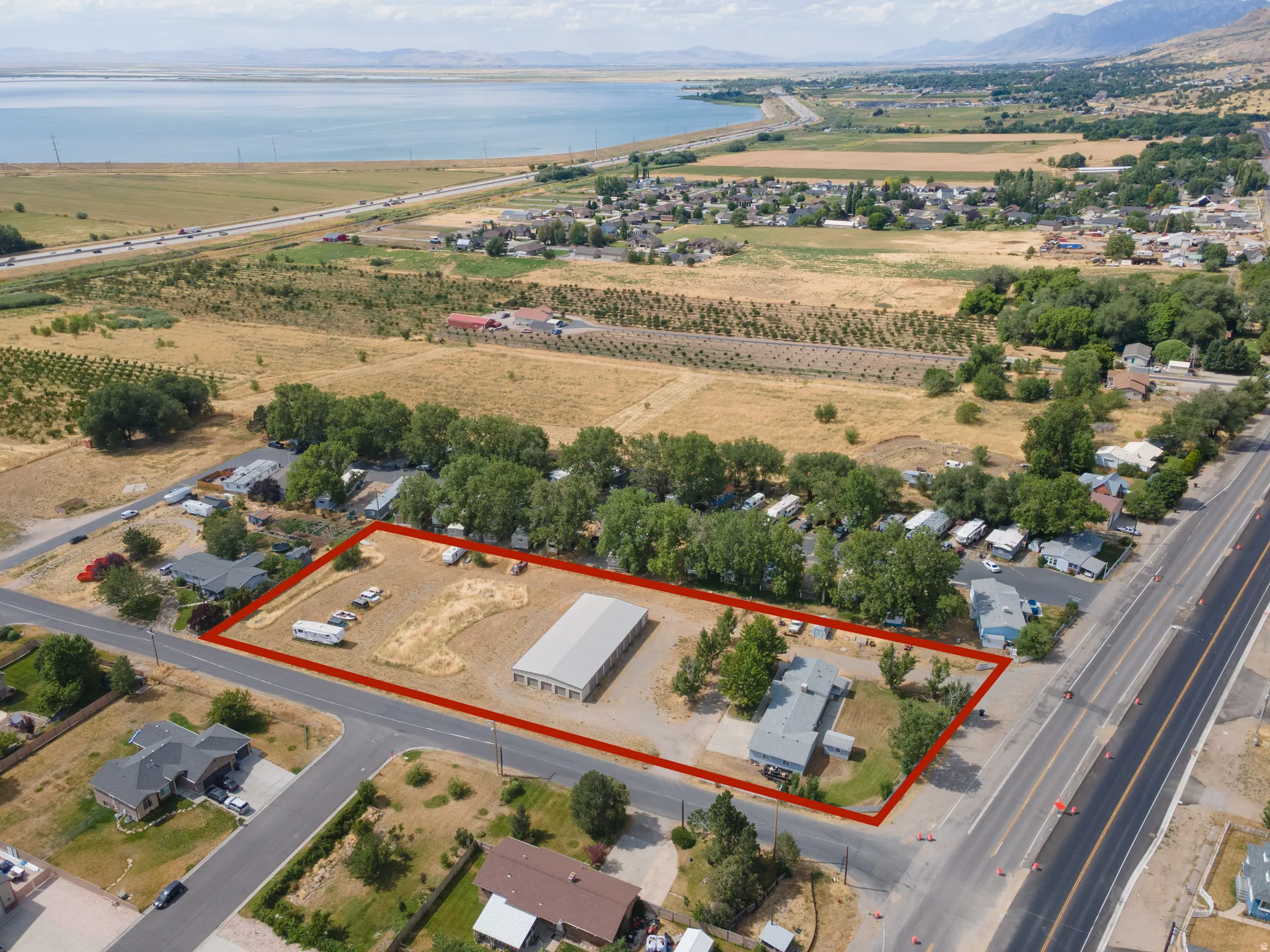 Expansive corner lot featuring a main residence, a large metal outbuilding, and additional paved and unpaved parking areas
