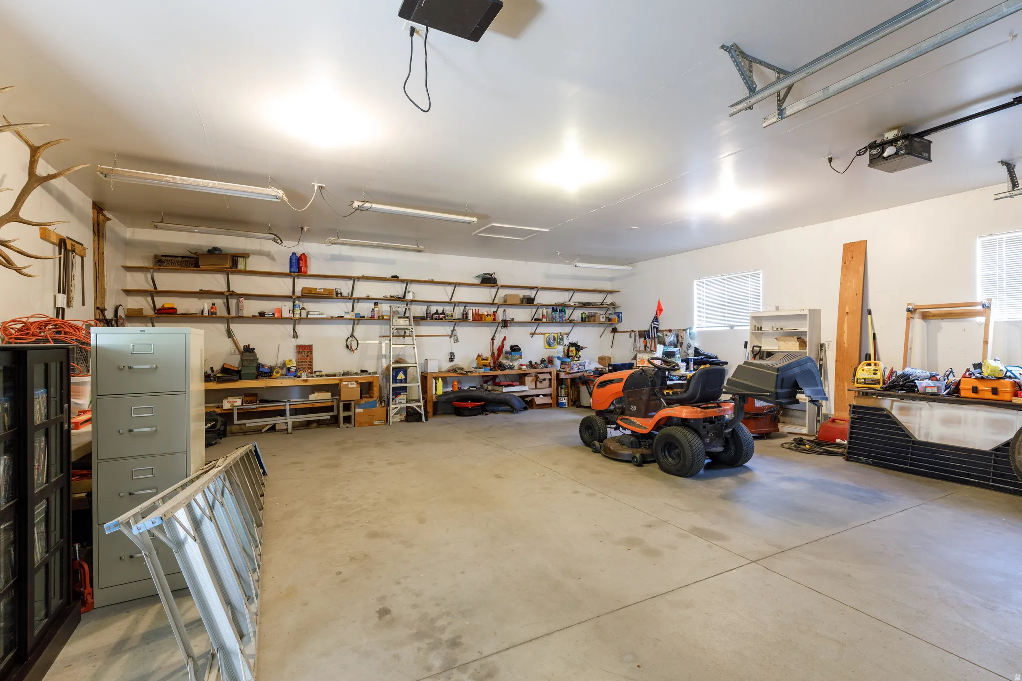 Spacious garage featuring a concrete floor, multiple windows, extensive built-in shelving, and overhead fluorescent lighting