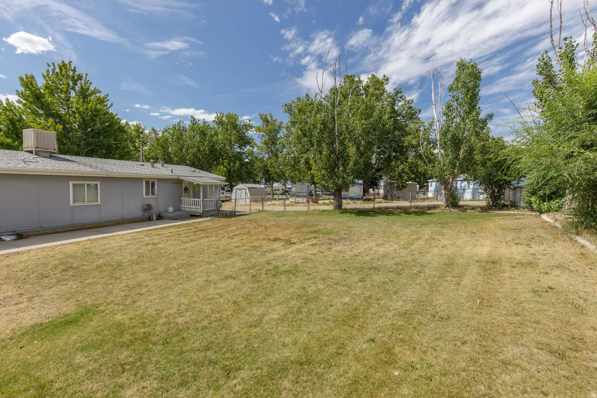 Expansive backyard featuring a large grass area, mature trees, and a partial fence