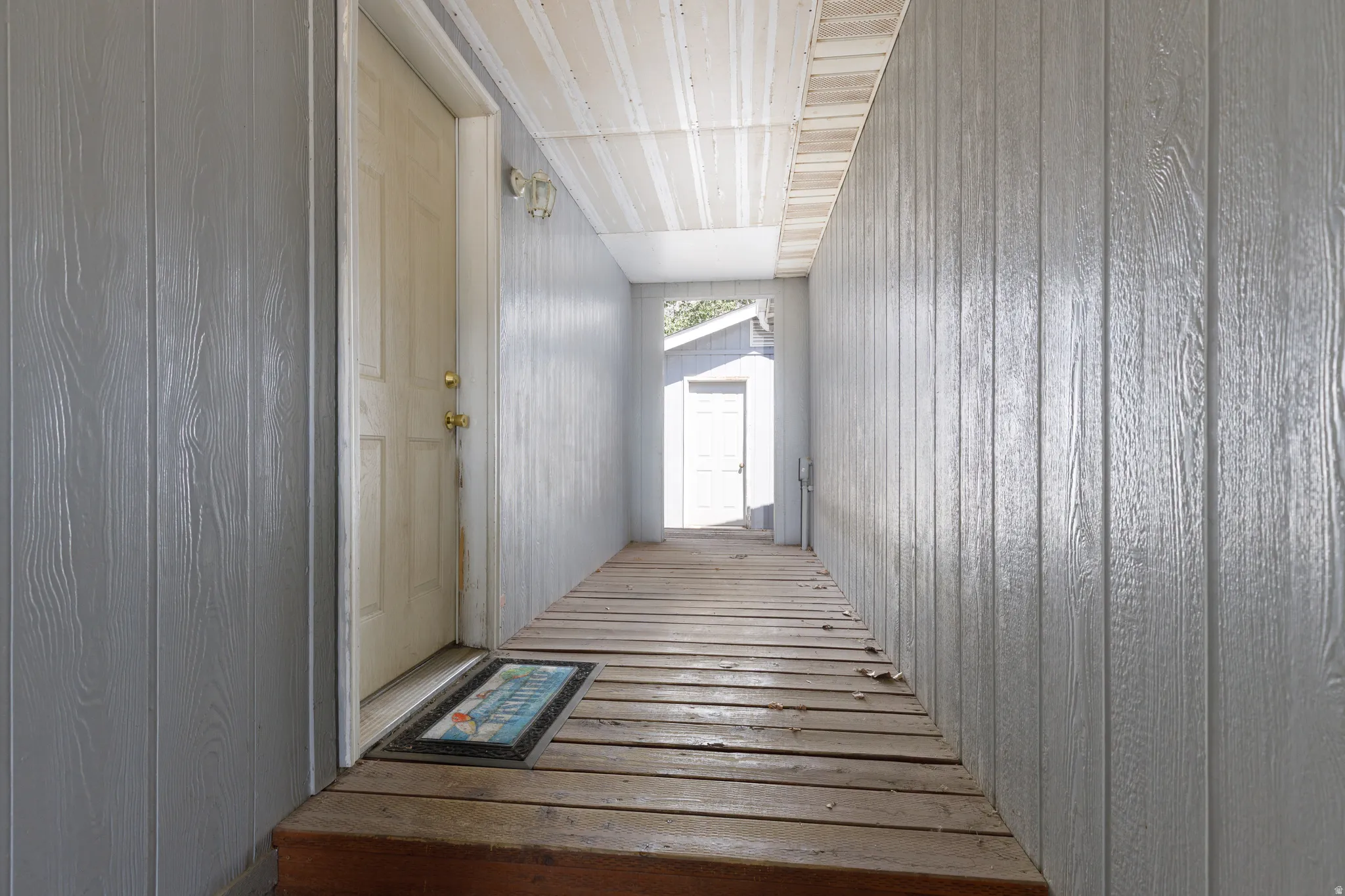 Covered exterior walkway featuring light gray paneled siding and wood plank flooring