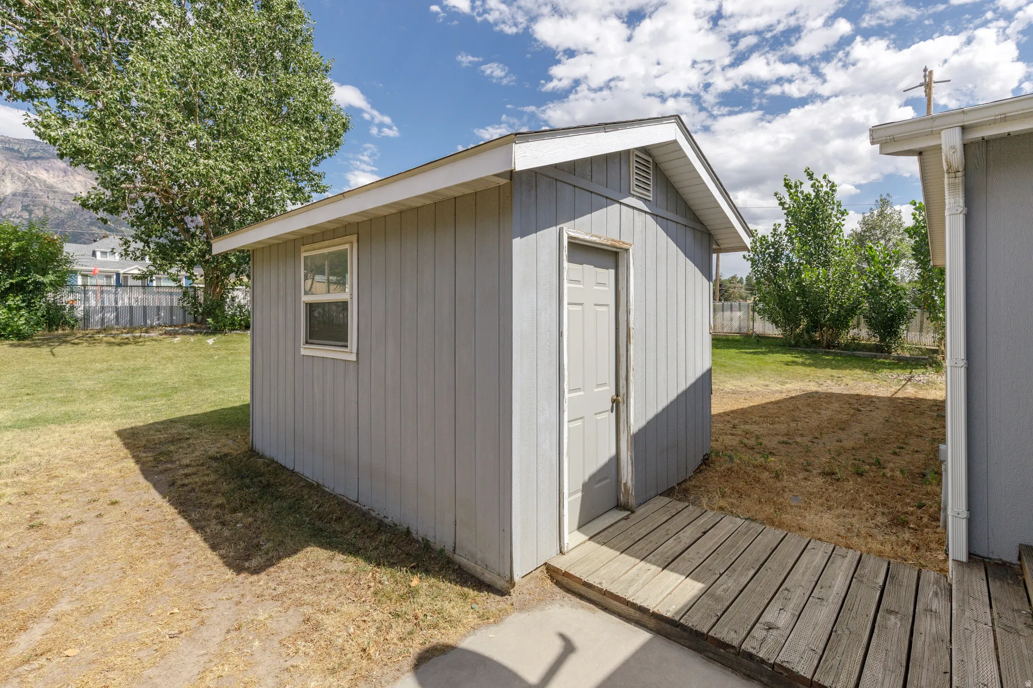 Detached storage shed with a panel door and a single window, featuring light gray siding and a white trim roofline
