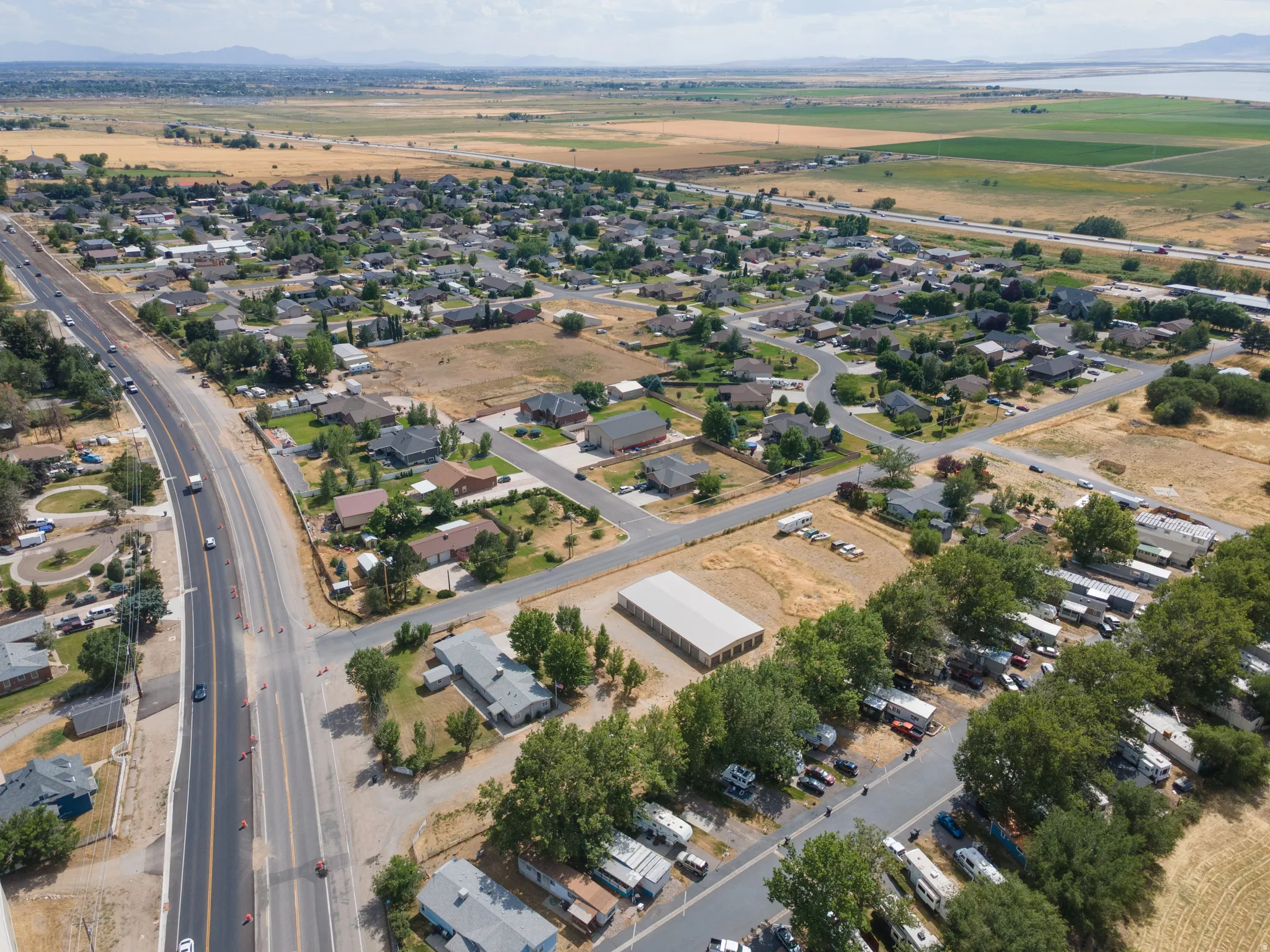 Aerial perspective showcasing a residential community with diverse housing styles, bordered by an active roadway and open fields