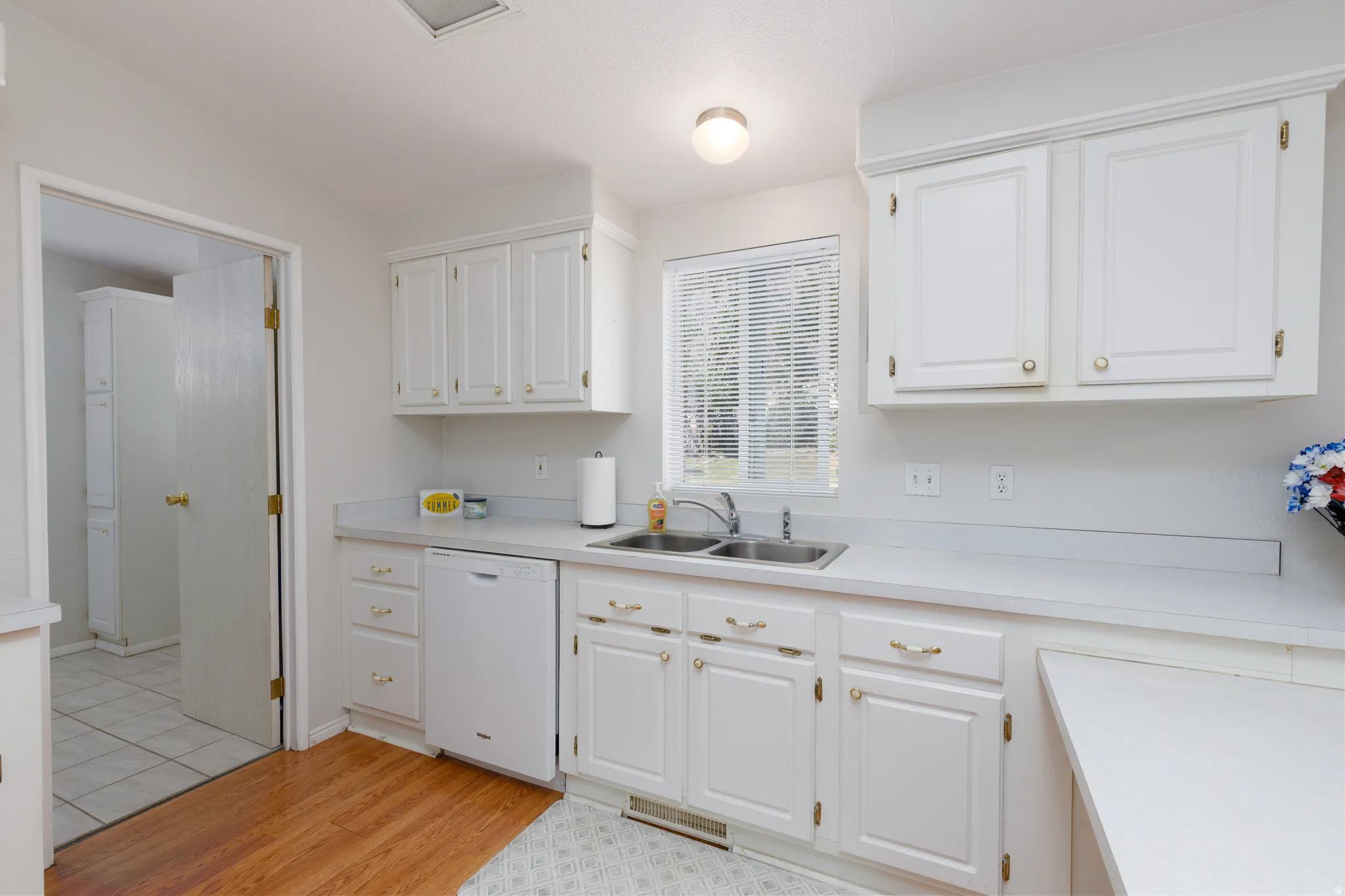 Kitchen featuring white cabinetry with gold-toned hardware, a double-basin stainless steel sink, and a built-in dishwasher