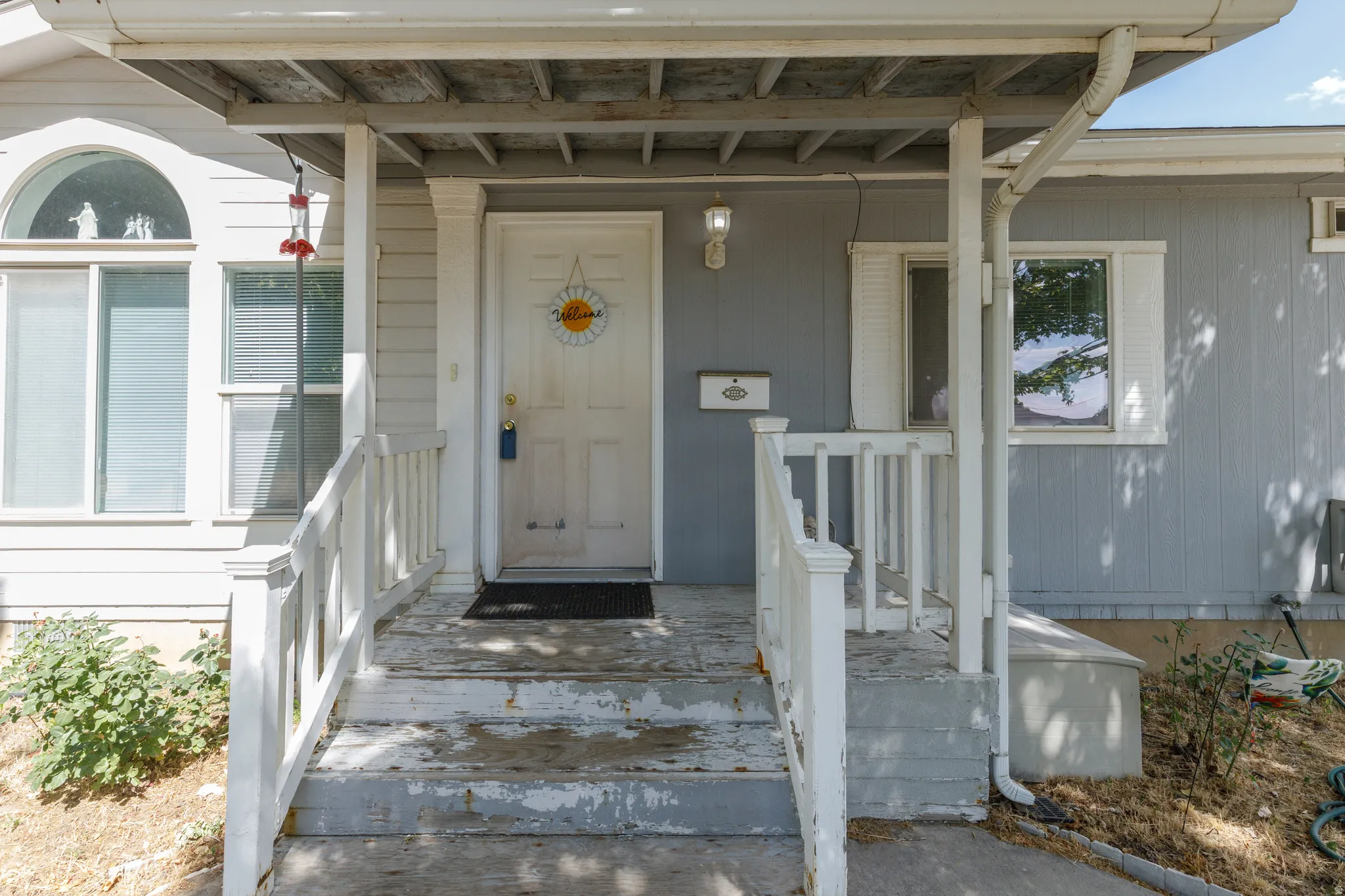 Front entry featuring a covered porch, white wood railing, and an arched window