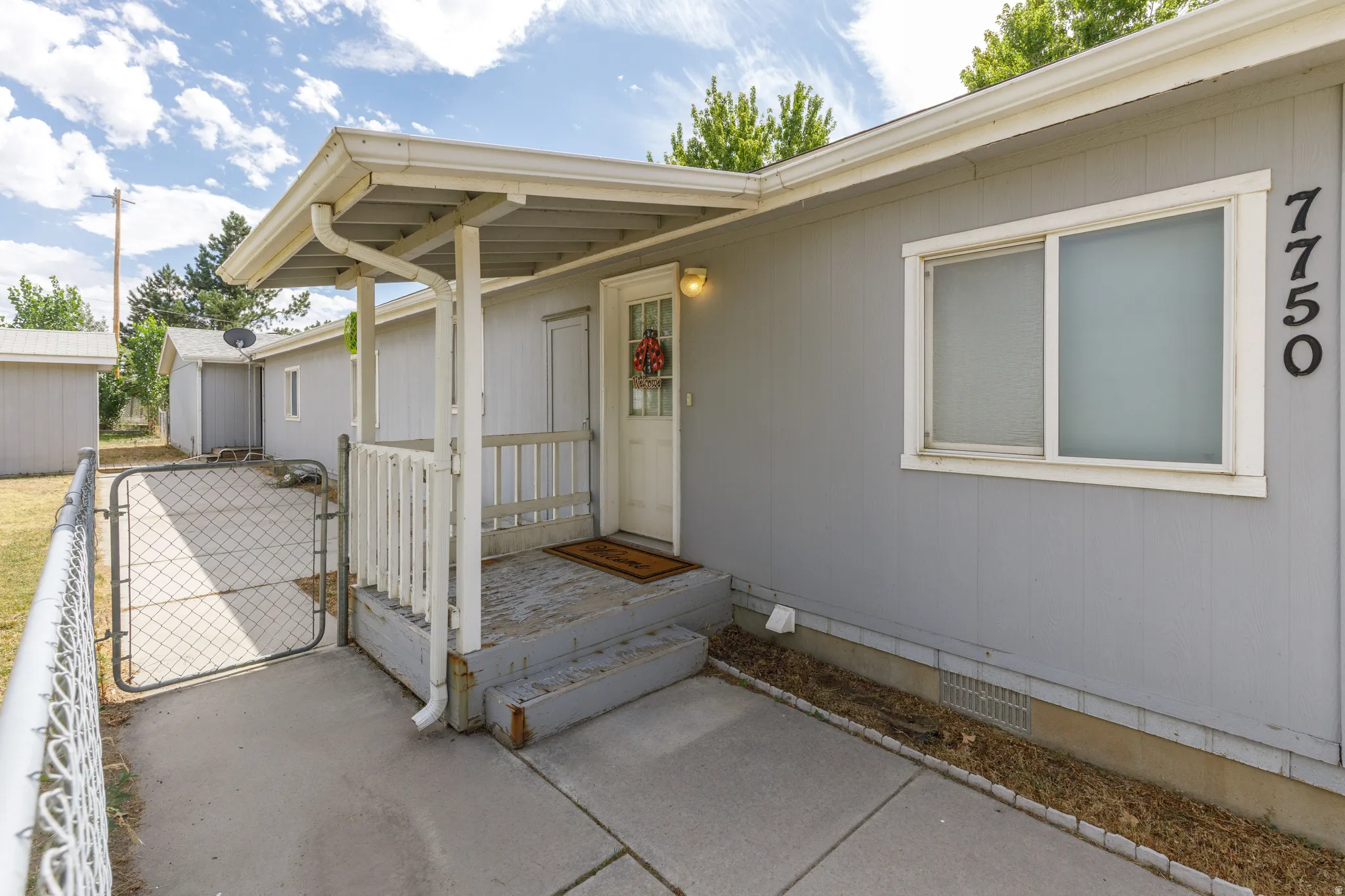 Covered entry porch with white railing, concrete walkway, and chain-link fencing