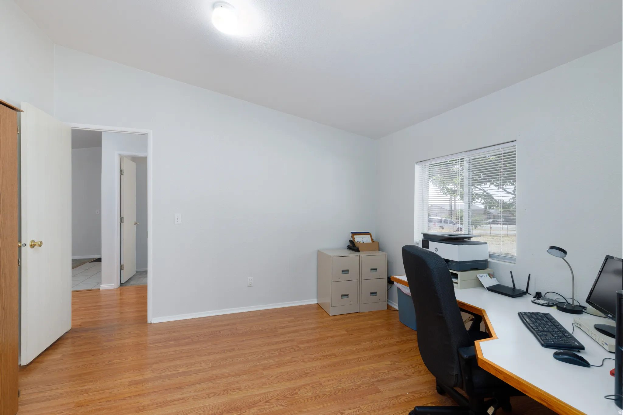 Spacious room featuring wood-finish flooring, light neutral wall paint, and a built-in window with horizontal blinds
