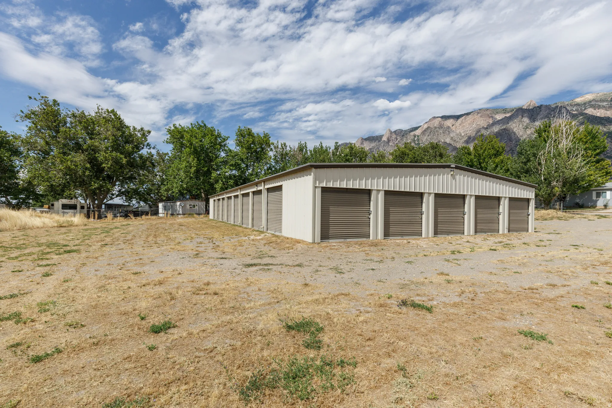Metal storage building featuring multiple roll-up doors, a light-colored corrugated exterior, and a dark roofline