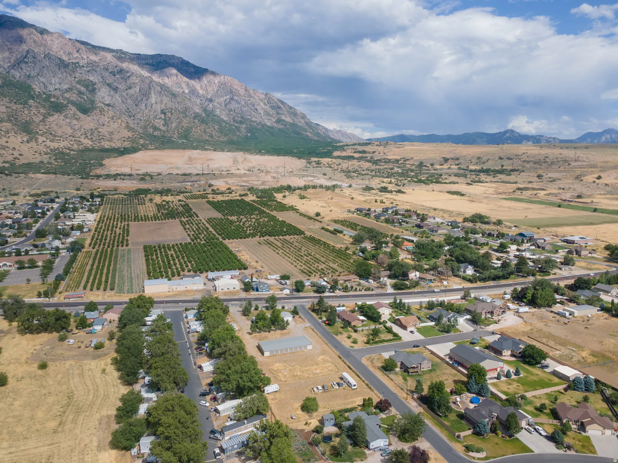 Expansive aerial perspective showcasing a mountainous backdrop, agricultural plots, residential areas with mature trees, and paved roadways