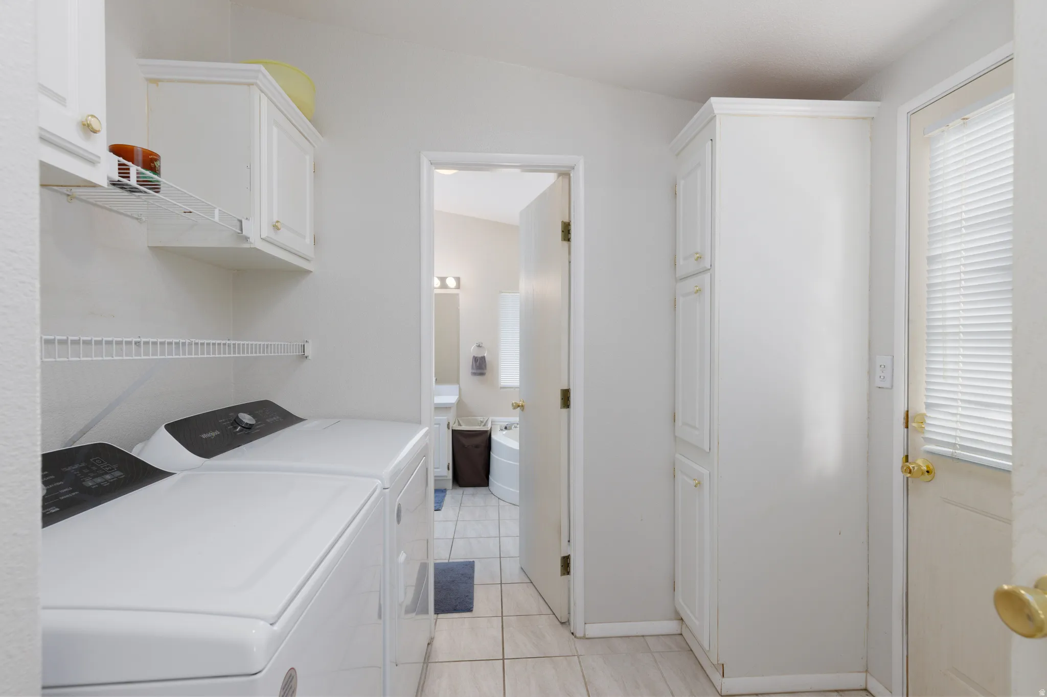 Dedicated laundry area featuring white cabinetry, wire shelving, and tile flooring