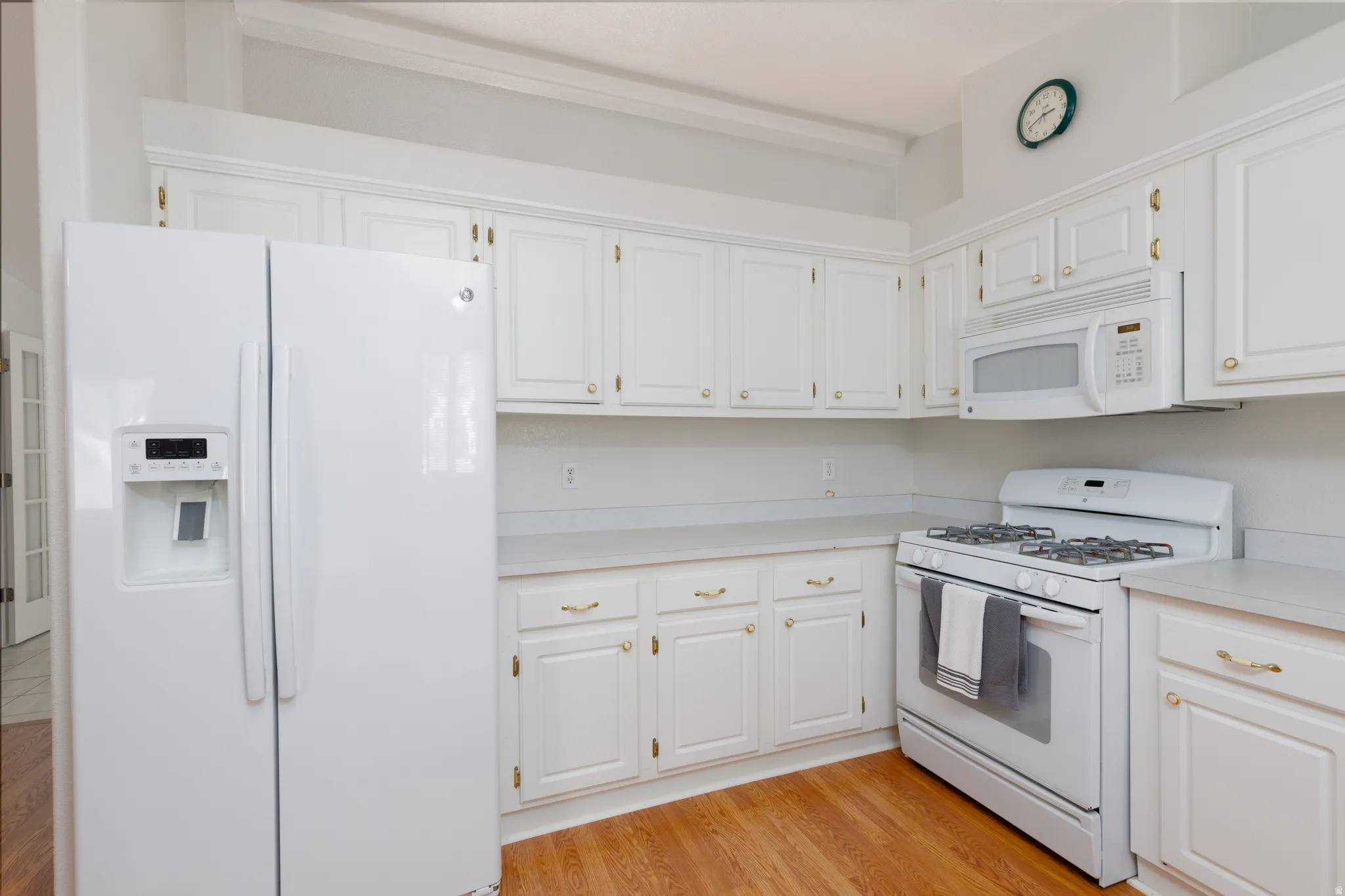 Kitchen featuring wood-finish flooring, white cabinetry with gold-tone hardware, white countertops, and white appliances including a gas range and built-in microwave