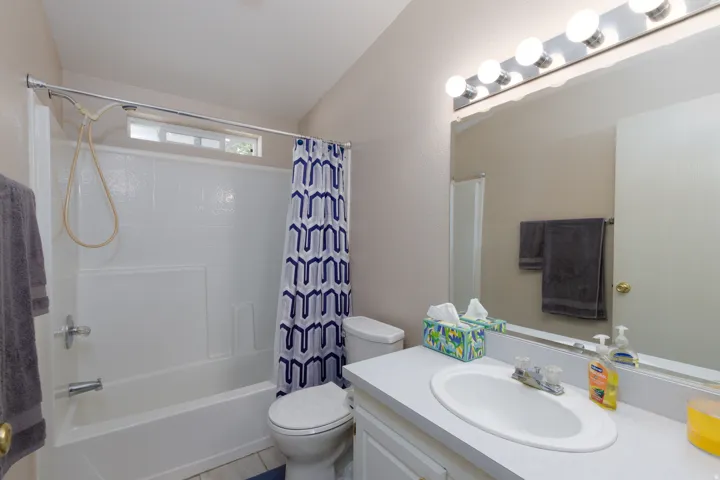 Bathroom featuring a bathtub with an integrated shower, a white vanity with a single sink, an expansive mirror, and overhead vanity lighting