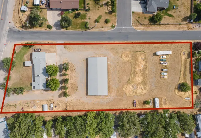 Expansive lot featuring a single-story residence, a large metal outbuilding, extensive unpaved areas, and mature trees